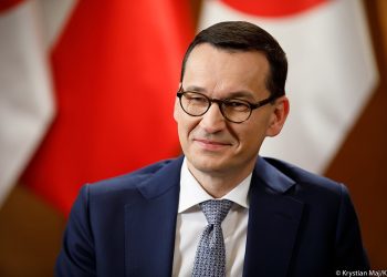 Premier Mateusz Morawiecki na tle flag
