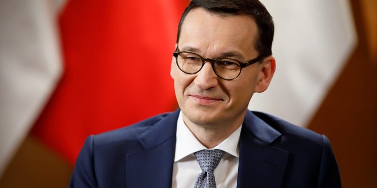 Premier Mateusz Morawiecki na tle flag
